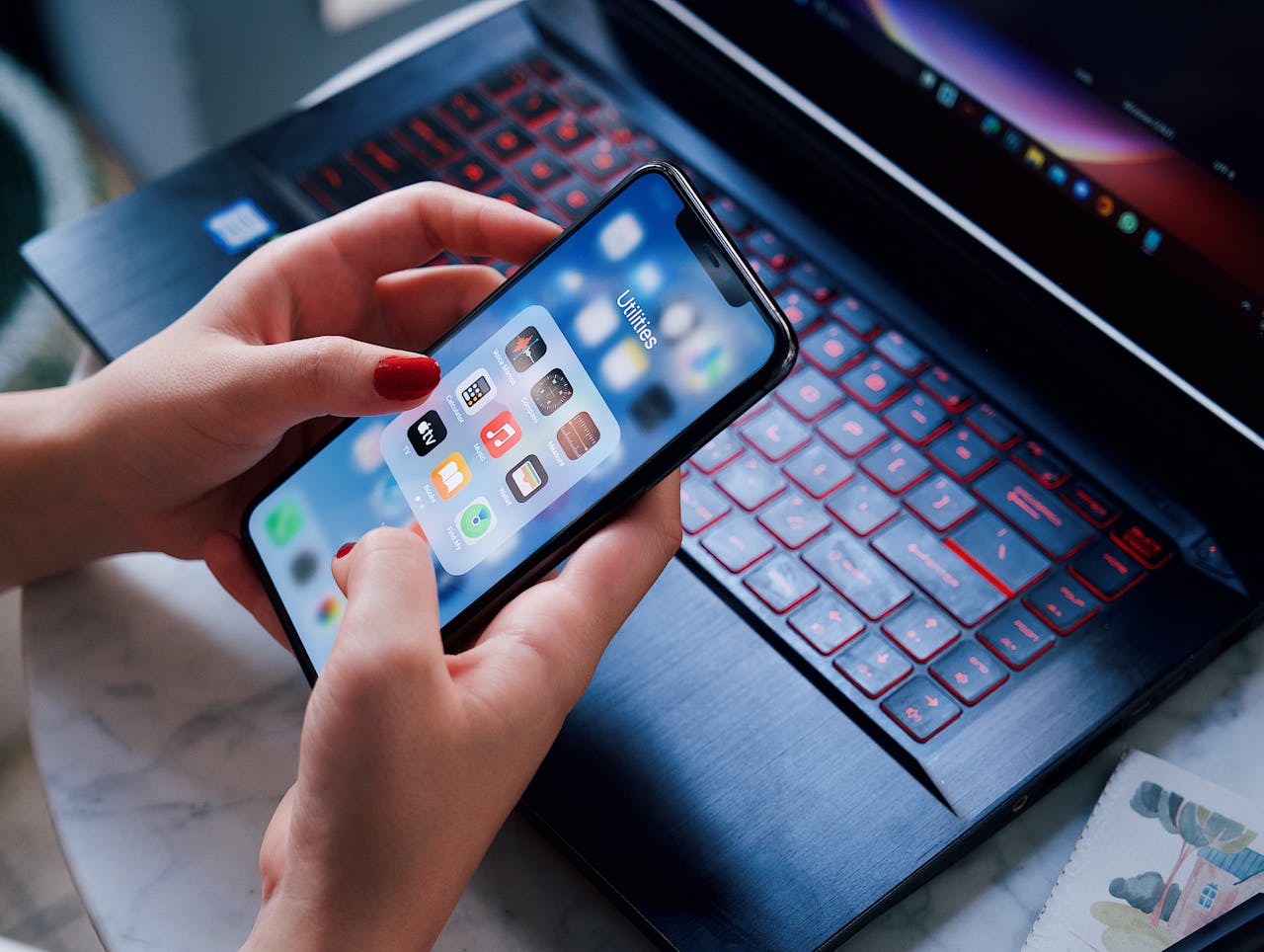 Close-up of a woman using a smartphone and laptop with red keyboard in an indoor setting.