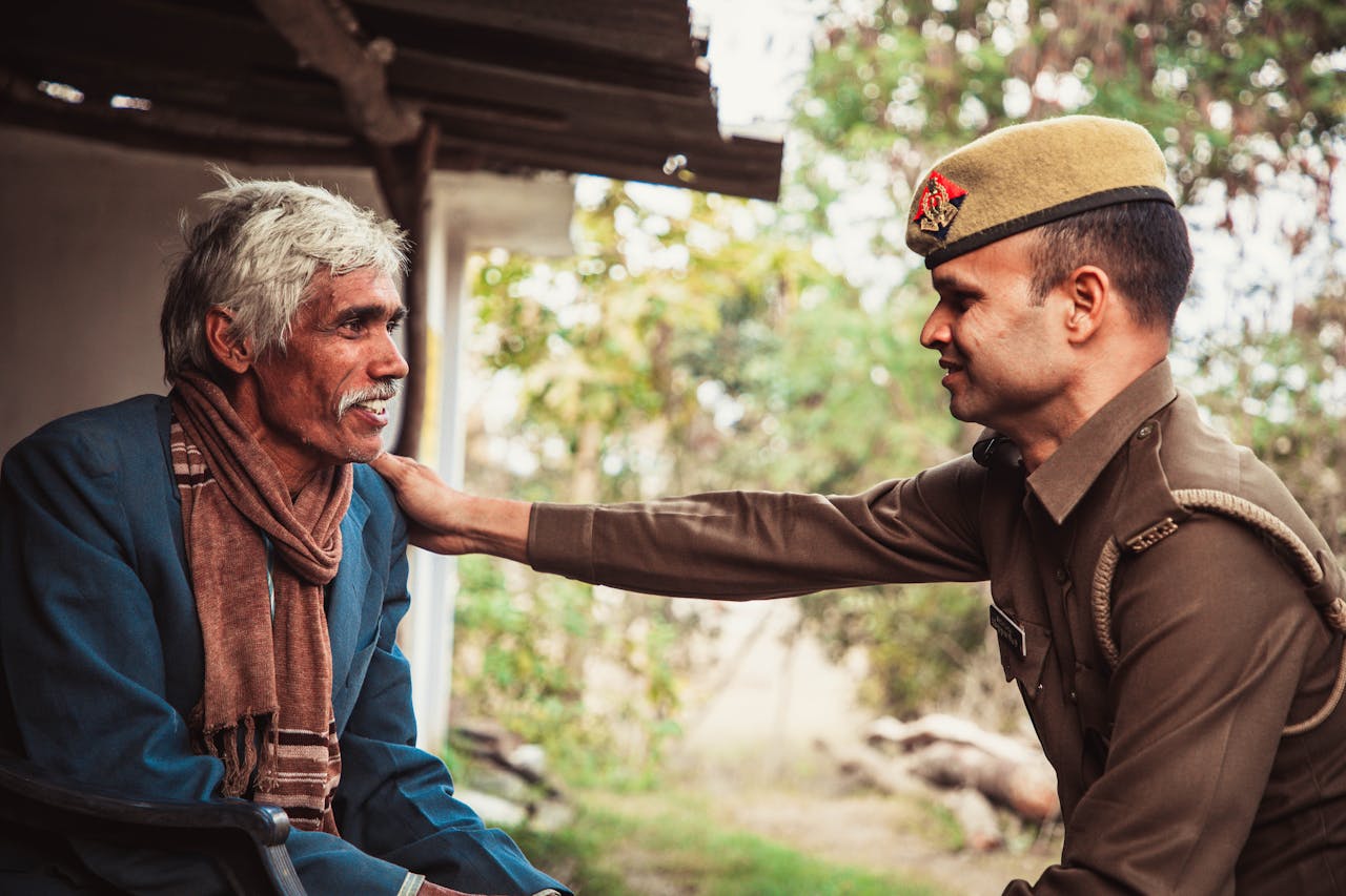 An elderly man smiling as a police officer offers a comforting gesture outdoors.